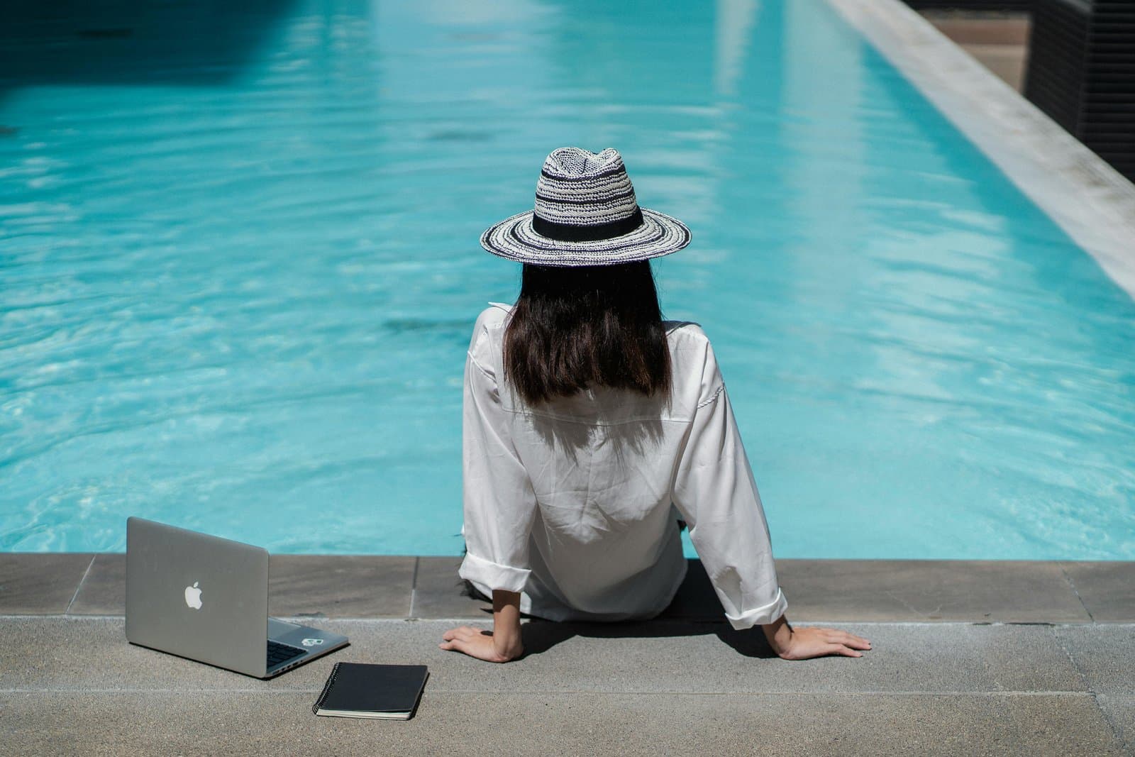 Digitale Nomadin arbeitet mit Laptop am Pool im Ausland