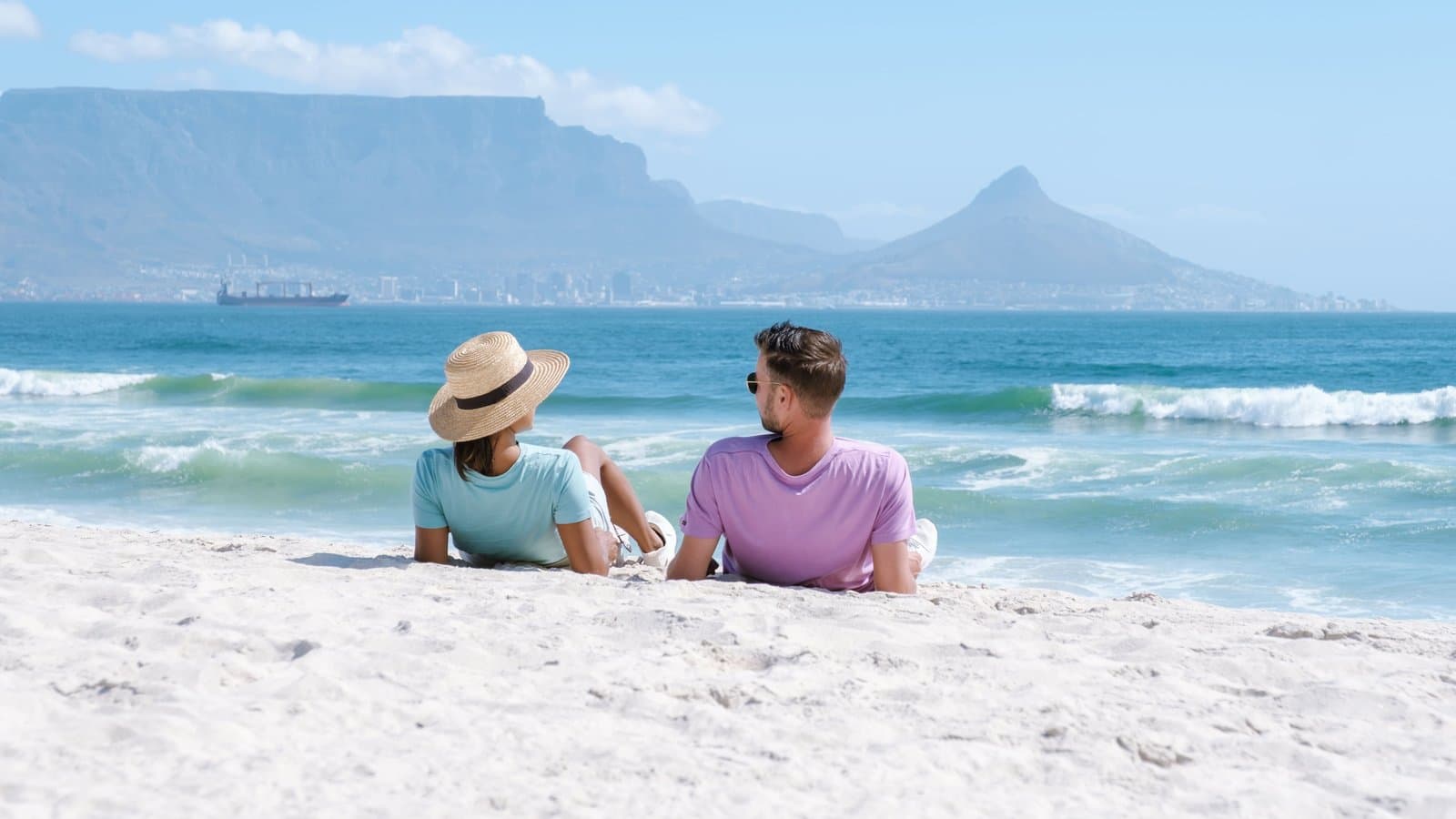 Paar liegt am Sandstrand in Südafrika mit Blick auf den Tafelberg