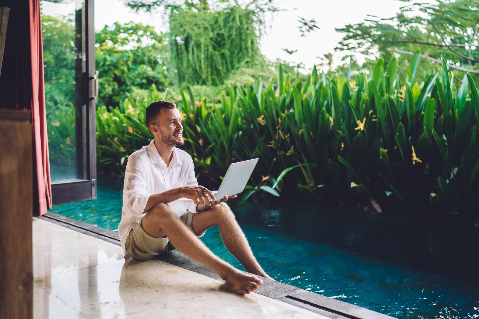 Digitaler Nomade arbeitet am Laptop neben dem Pool seiner Villa in Indonesien